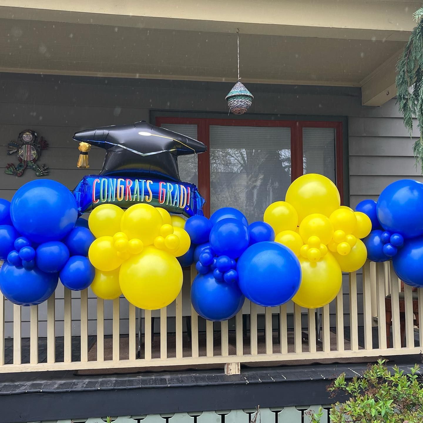 A balcony decorated with blue and yellow balloons and a graduation cap