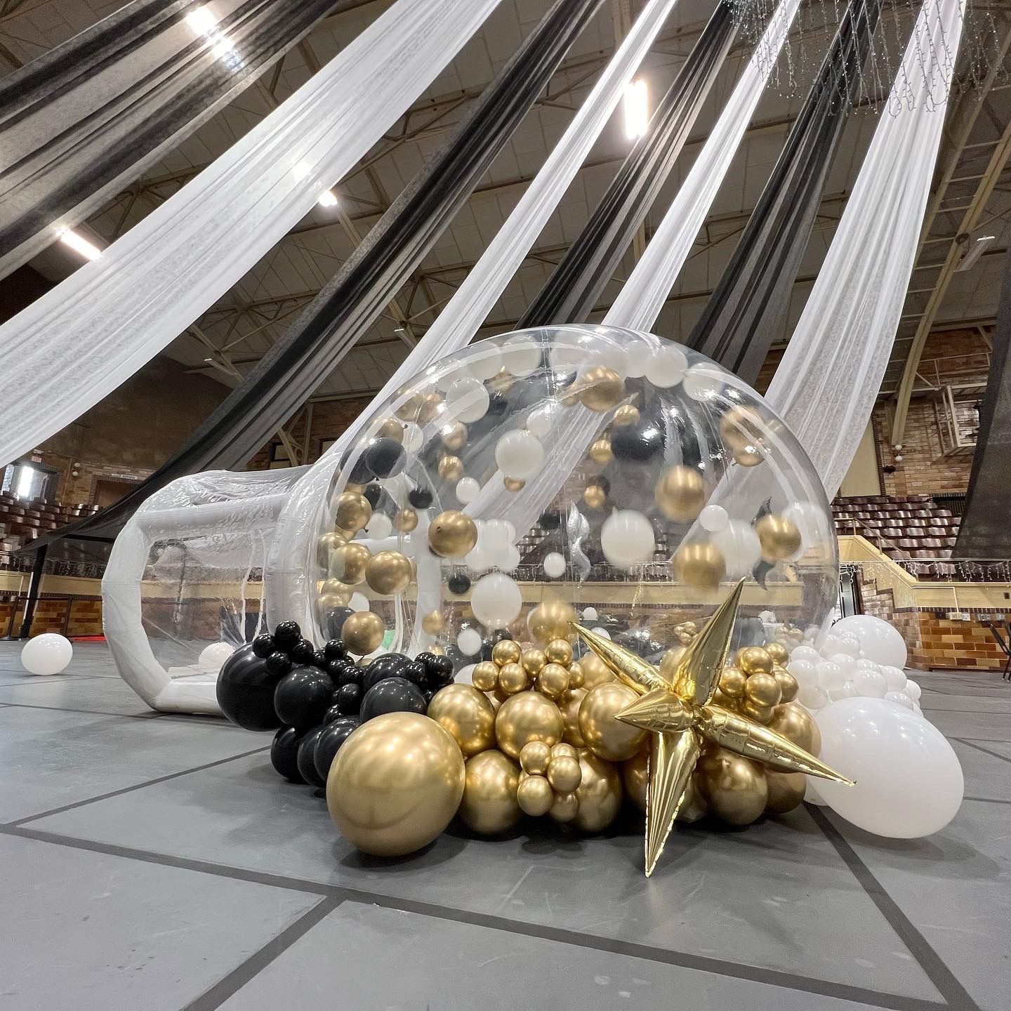 A balloon filled climb inside snow globe with balloon garland in chrome gold white and black