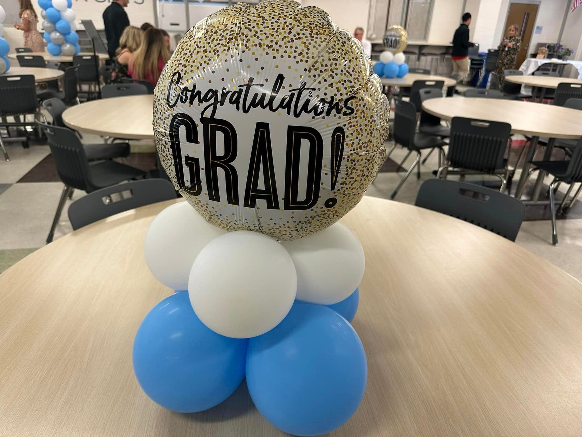 A congratulations grad balloon is sitting on top of a table surrounded by blue and white balloons.