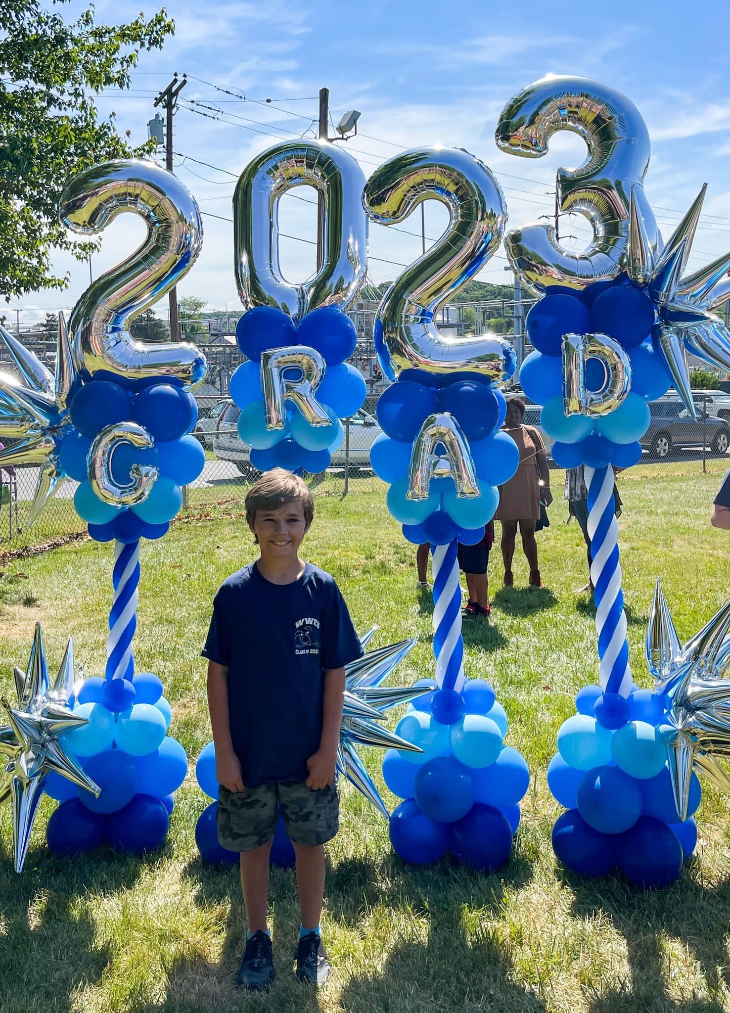 A young boy is standing in front of a display of balloons for a graduation ceremony.