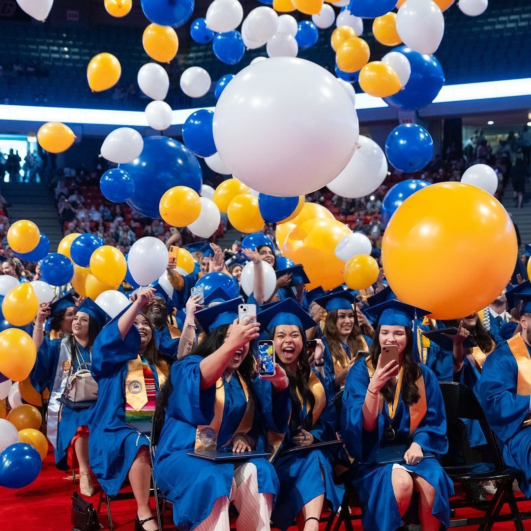 A group of graduates are sitting under a bunch of balloons