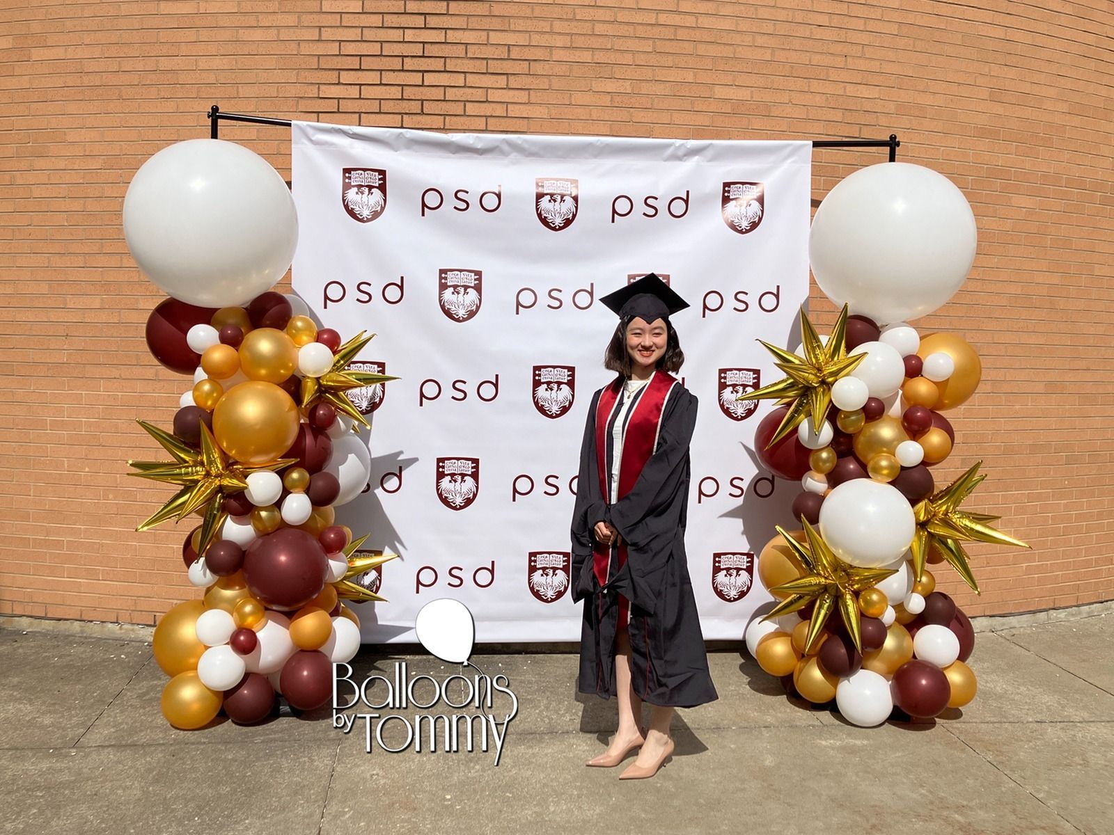 A woman in a graduation cap and gown is standing in front of balloons.
