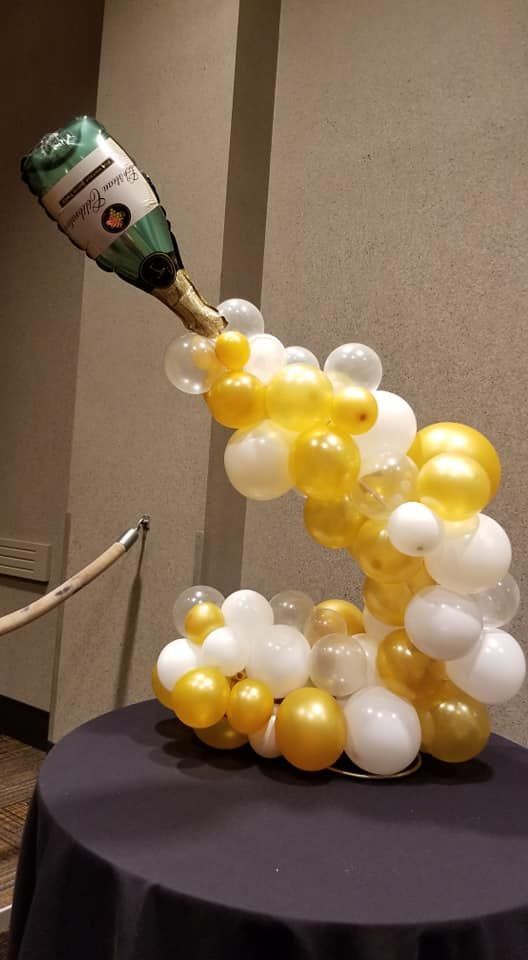 A bottle of champagne is being poured out of a balloon on a table.