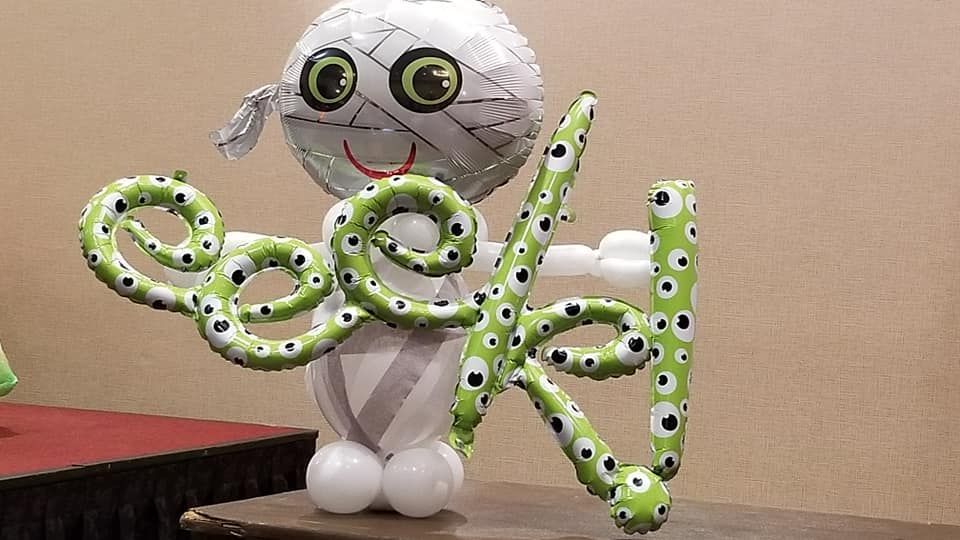 A mummy made out of balloons is holding a green octopus.