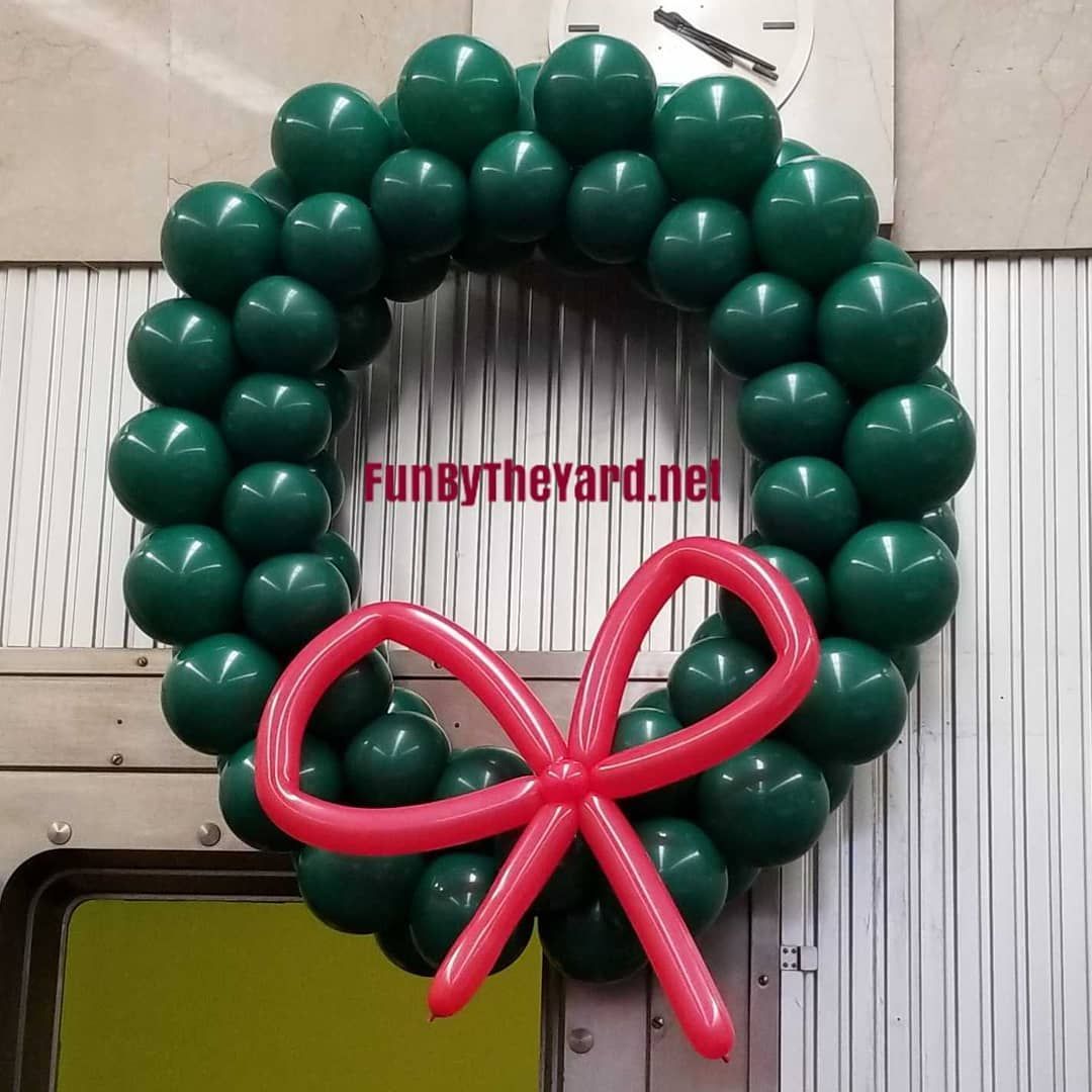 A wreath made of green balloons with a red bow