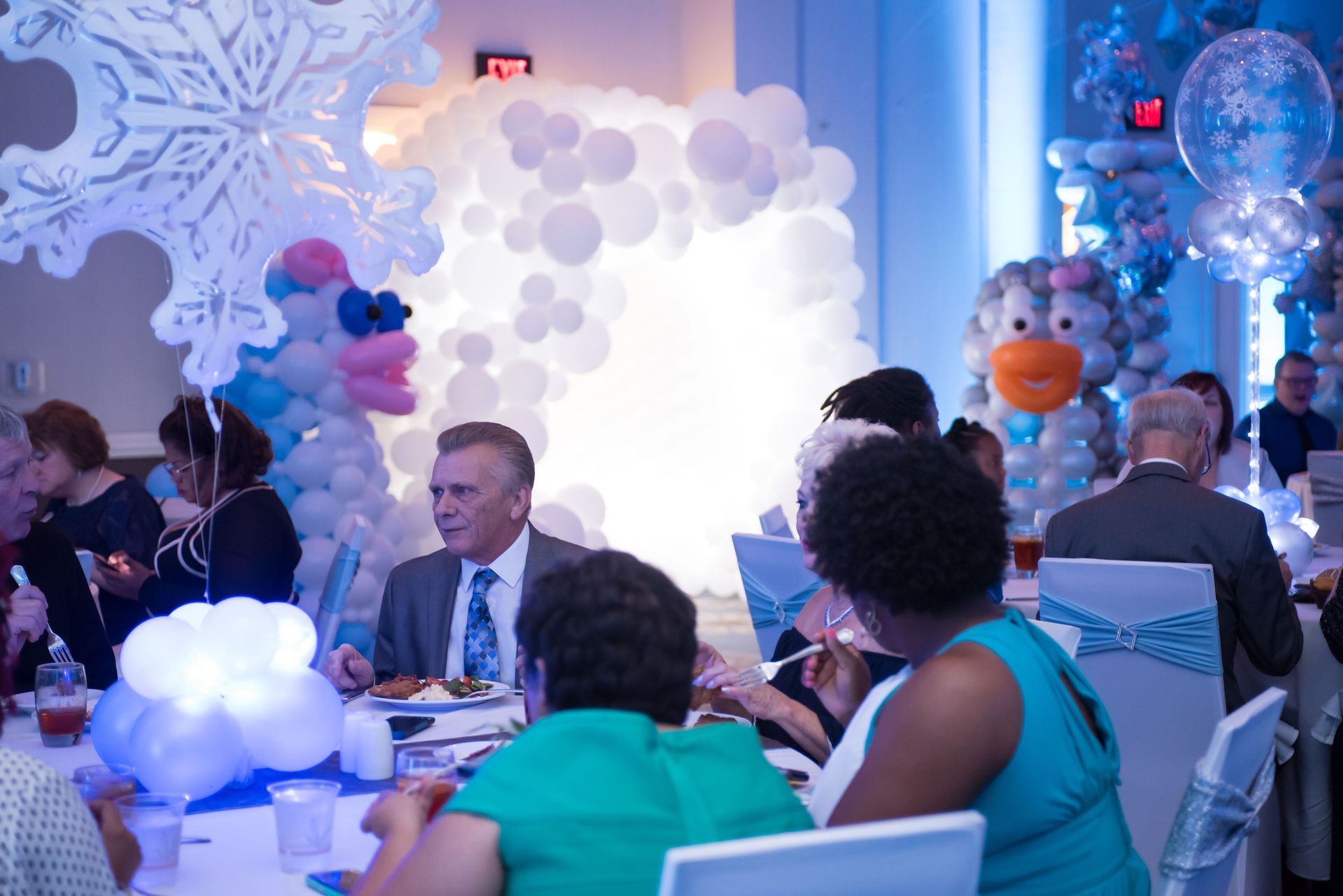 A group of people are sitting at tables in a room decorated with balloons.