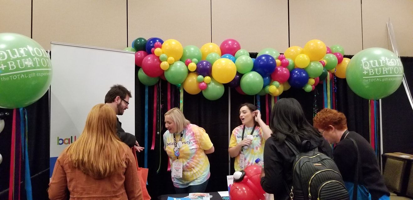 A group of people are standing around a table with balloons. Tradeshow balloons