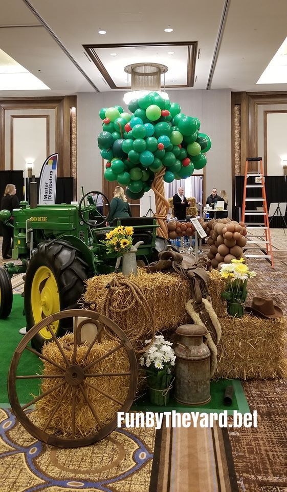 A tractor is sitting next to a hay bale and a tree made of balloons.