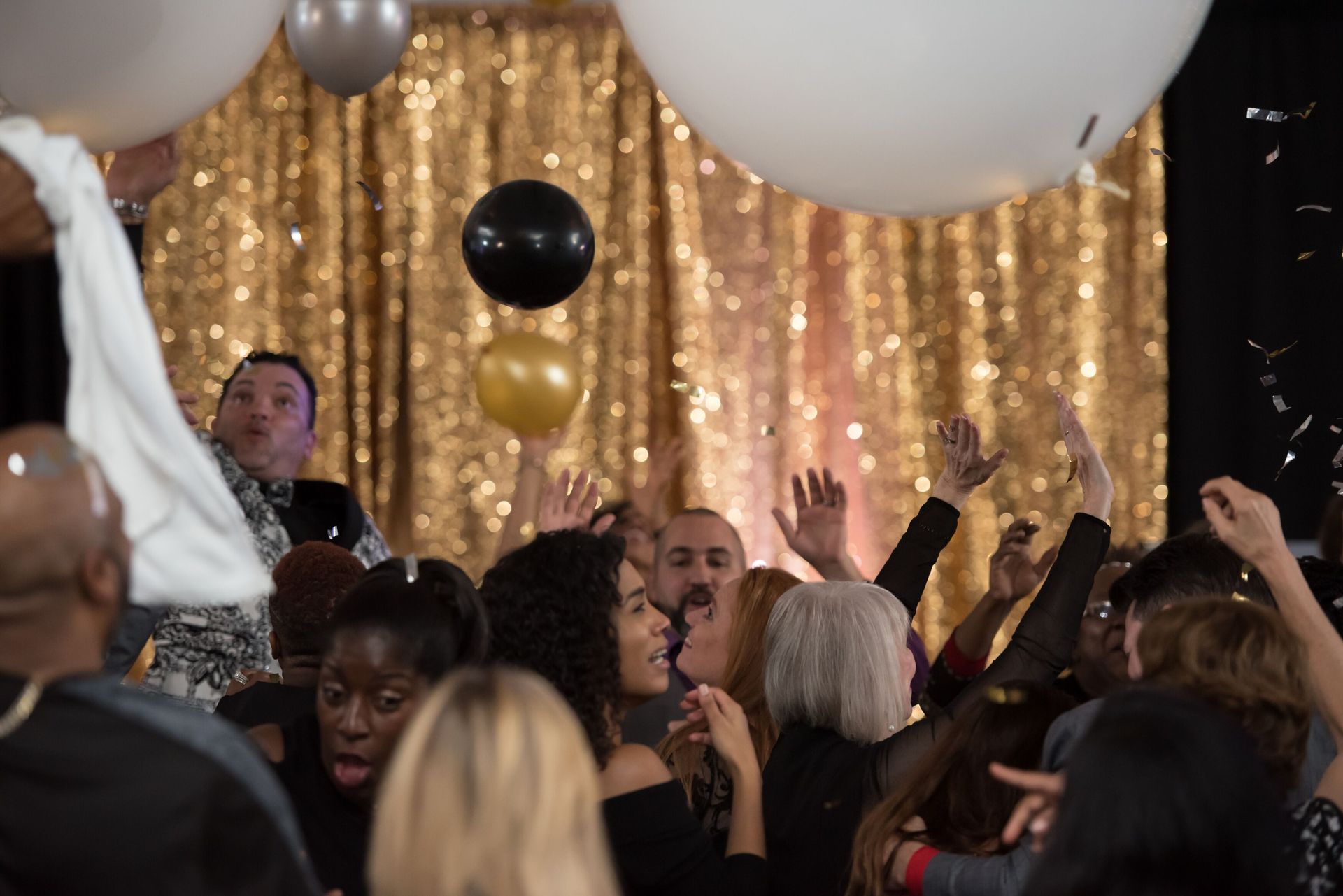 A crowd of people are dancing at a party with balloons and confetti. Balloon drop