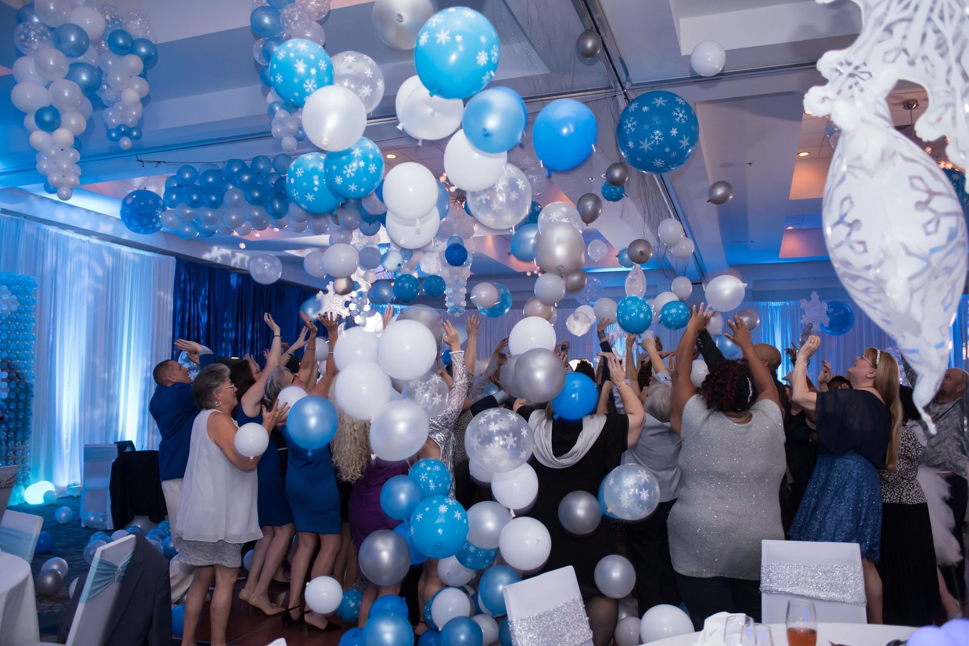 A group of people are dancing in a room filled with balloons.  Balloon Drop
