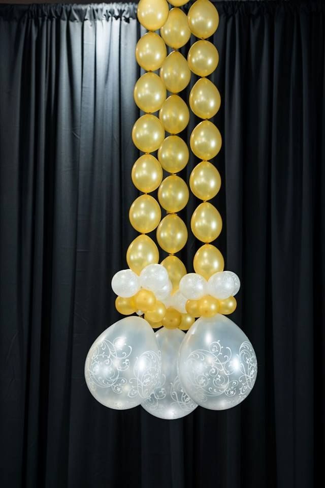 A string of gold and white balloons hanging from a black curtain.