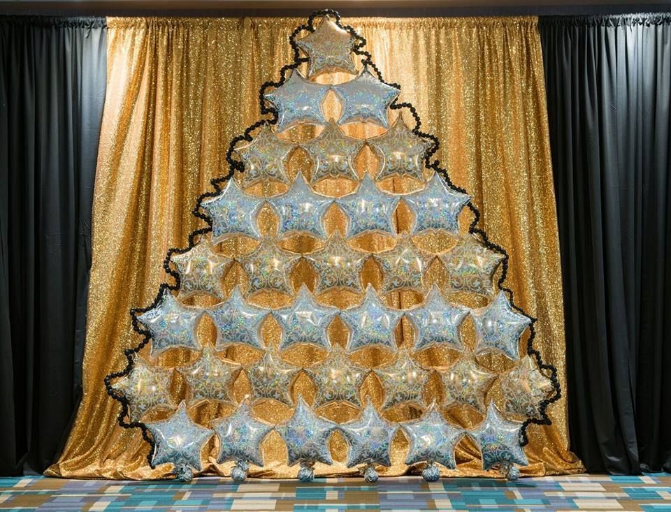 A christmas tree made out of balloons is sitting in front of a gold curtain.