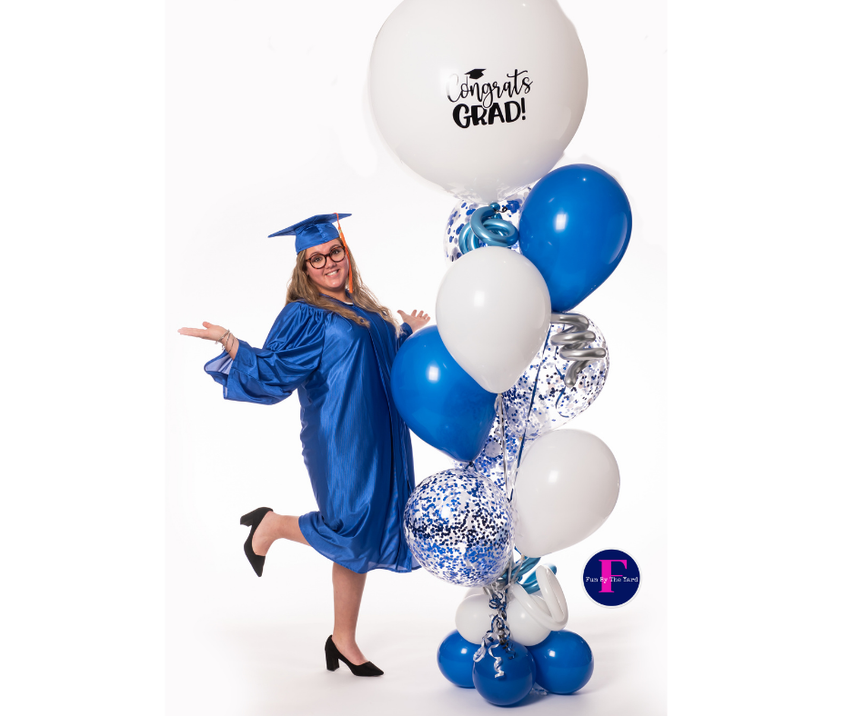 A woman in a graduation cap and gown is standing next to a bunch of blue and white balloons.