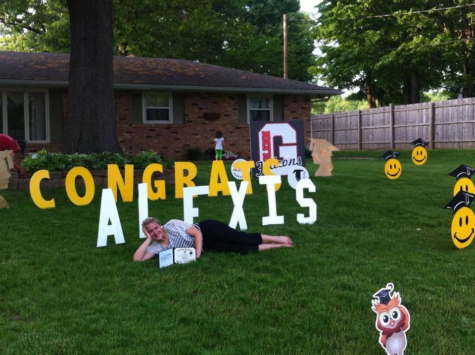 A woman laying on the grass in front of a sign that says congrats alexis