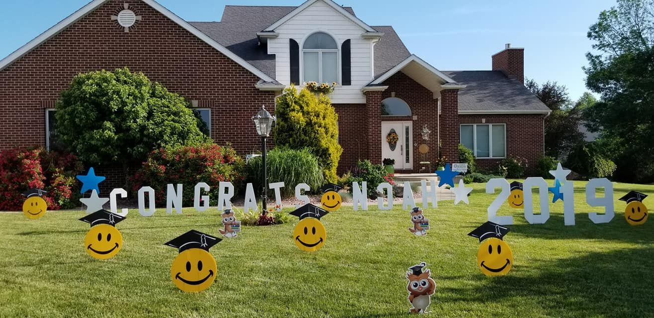 A brick house with a lawn decorated with graduation signs and smiley faces.