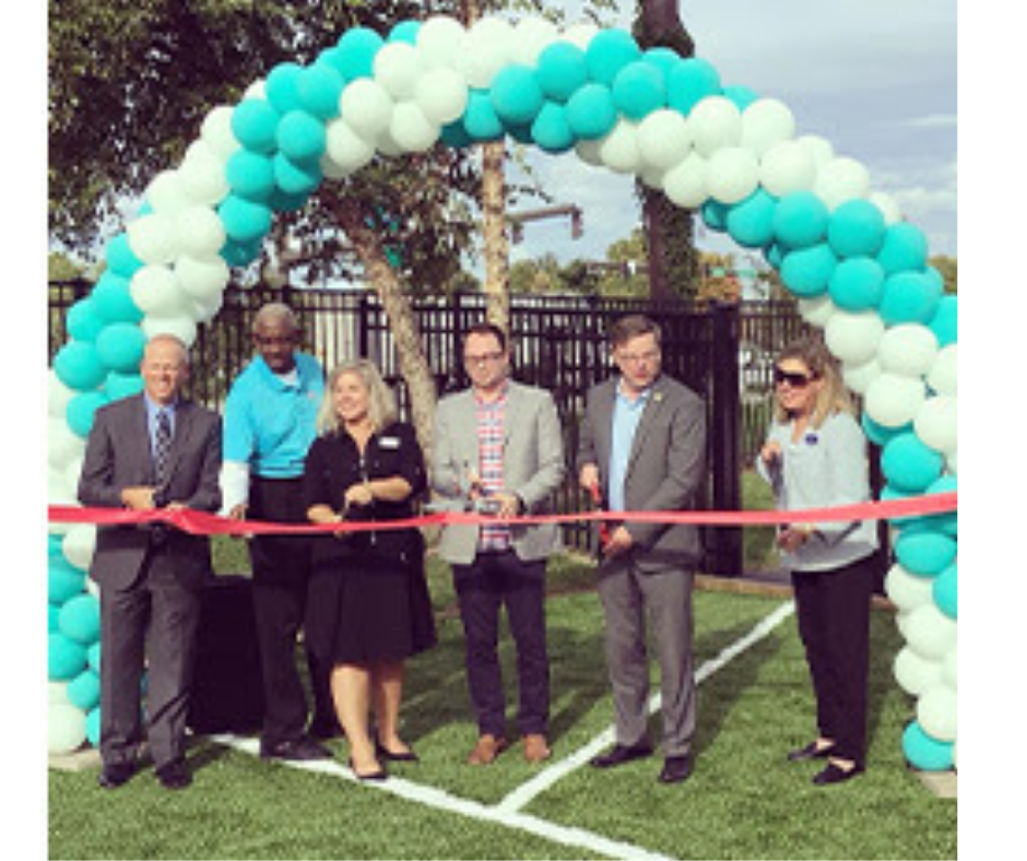 A group of people are cutting a red ribbon in front of a balloon arch for a grand opening