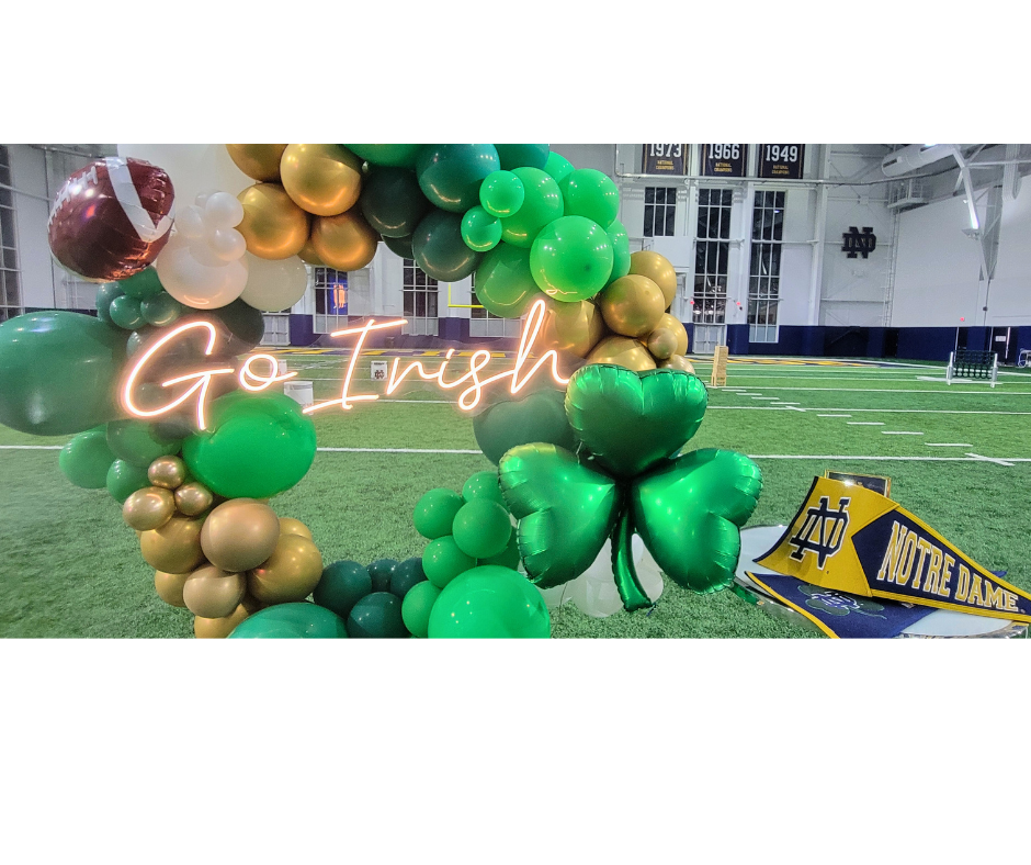 A football field decorated with green and gold balloons and a neon sign that says `` go irish ''.