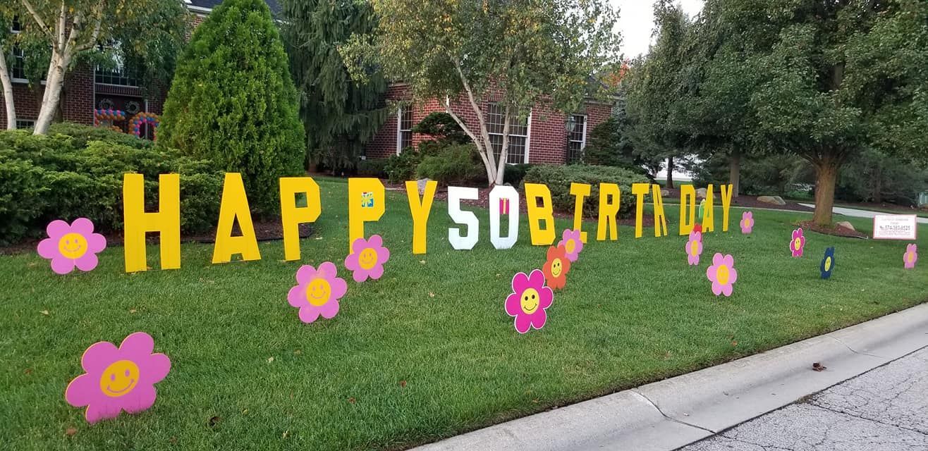 A happy 50th birthday sign in a yard with flowers.