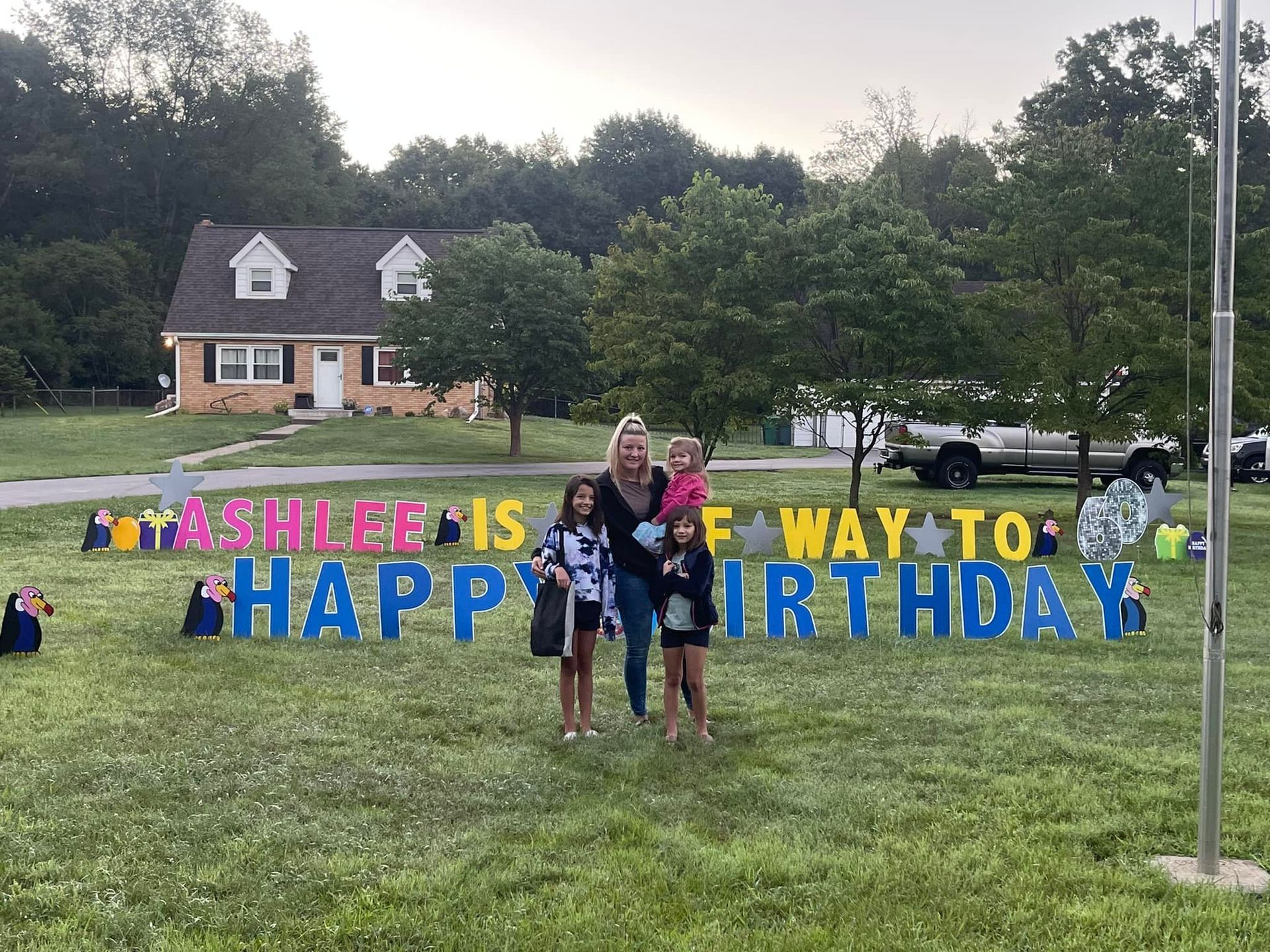 A woman and three children are standing in front of a happy birthday sign.