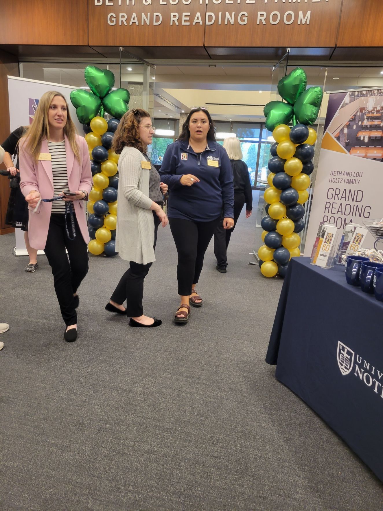 three women are walking through a room with balloons and a sign that says grand reading room
