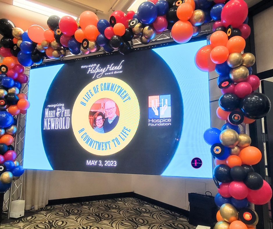 A large screen is surrounded by balloons in a room.