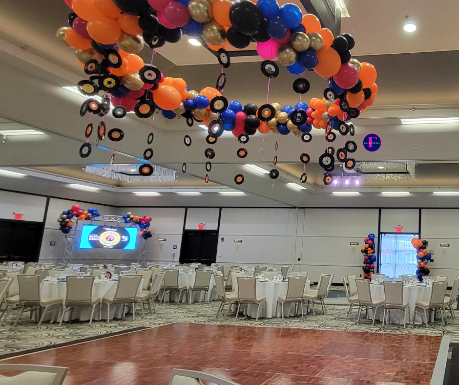 A large room with tables and chairs and balloons hanging from the ceiling