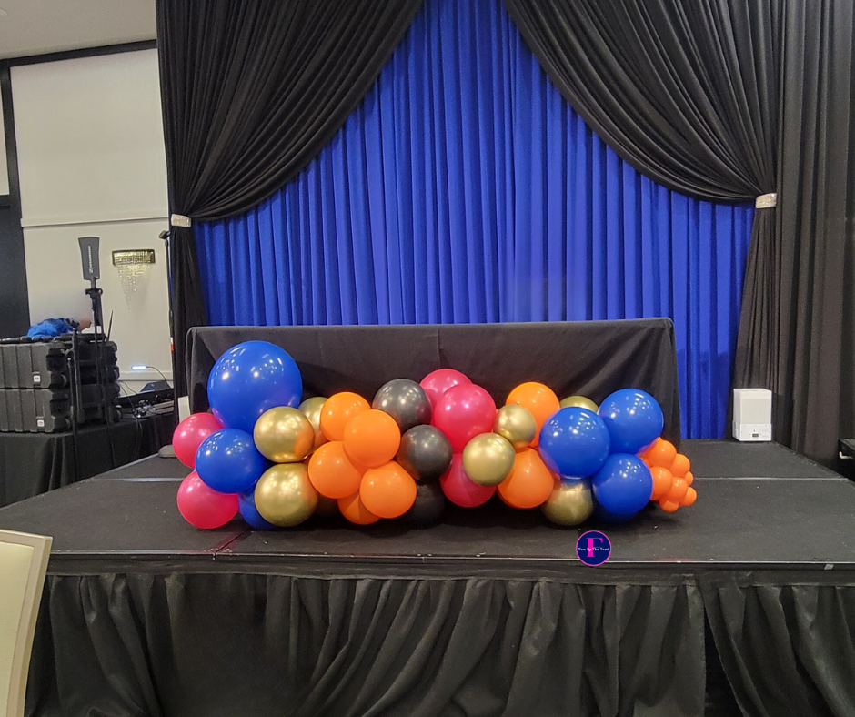 An organic balloon garland on a stage in front of a blue curtain.