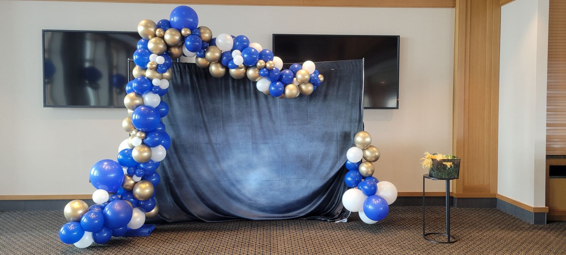 A room decorated with blue and gold balloons and a black curtain.