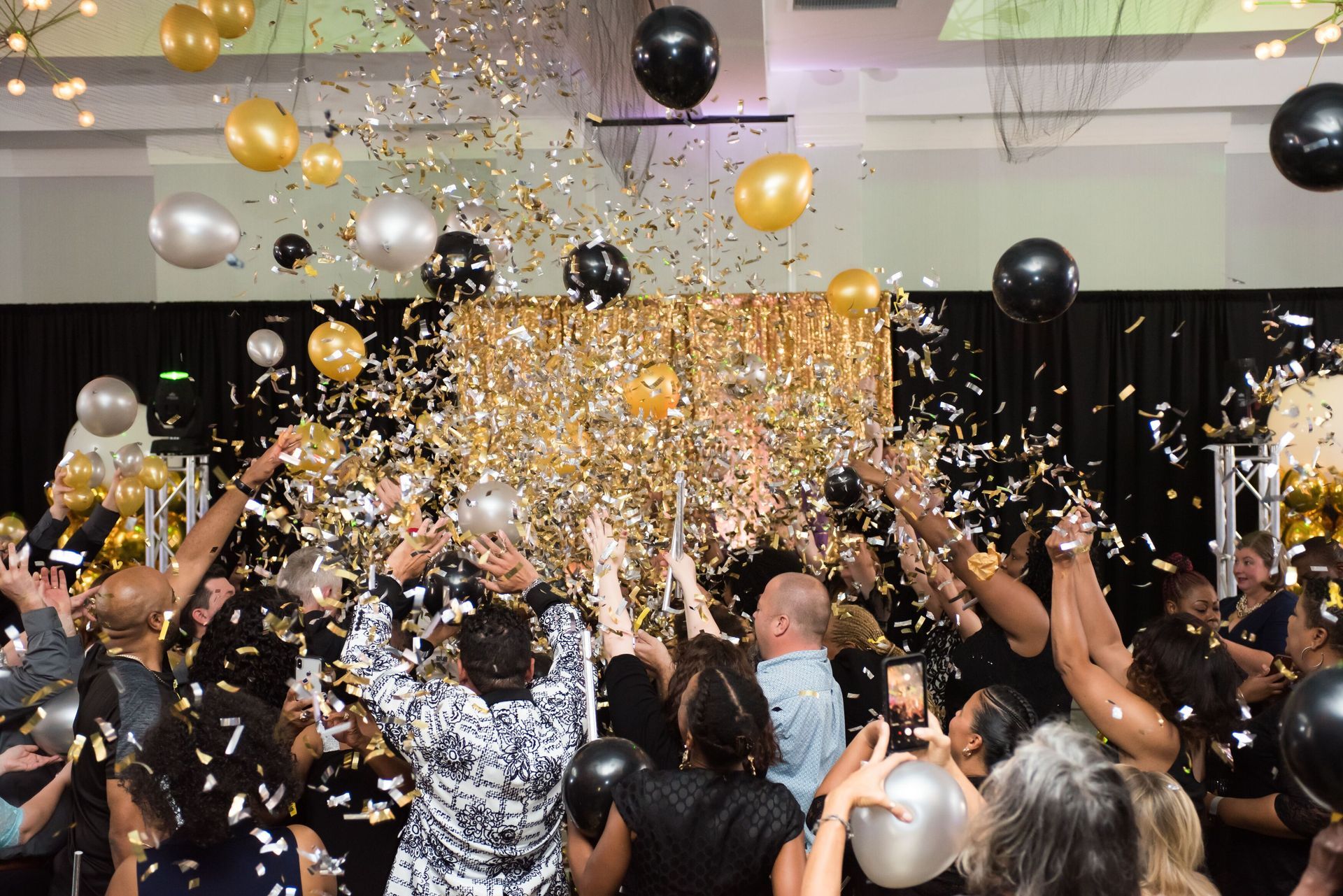 A crowd of people are throwing confetti and balloons at a party.