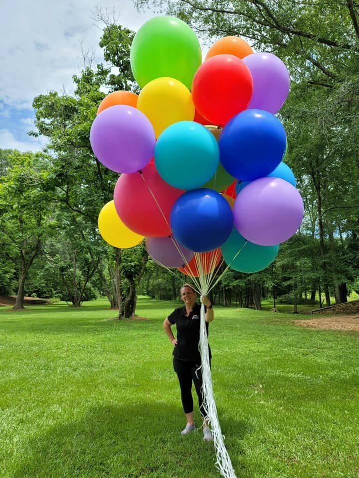 A woman is holding a bouquet of colorful balloons in a park.