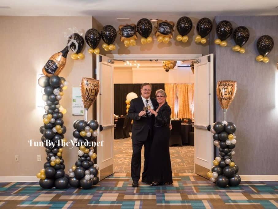 A man and woman are standing in front of a door decorated with balloons.