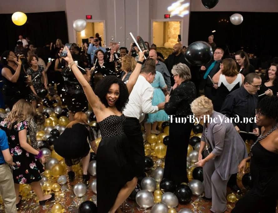 A woman in a black dress is surrounded by balloons at a party sponsored by funbytheyard.net