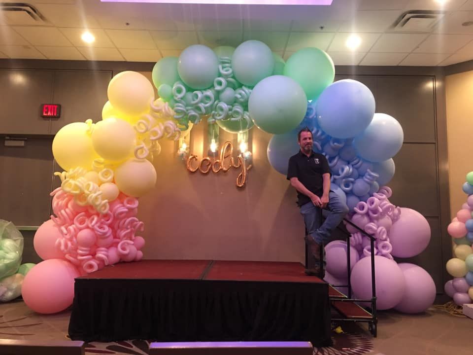 A man is standing in front of a stage decorated with balloons.