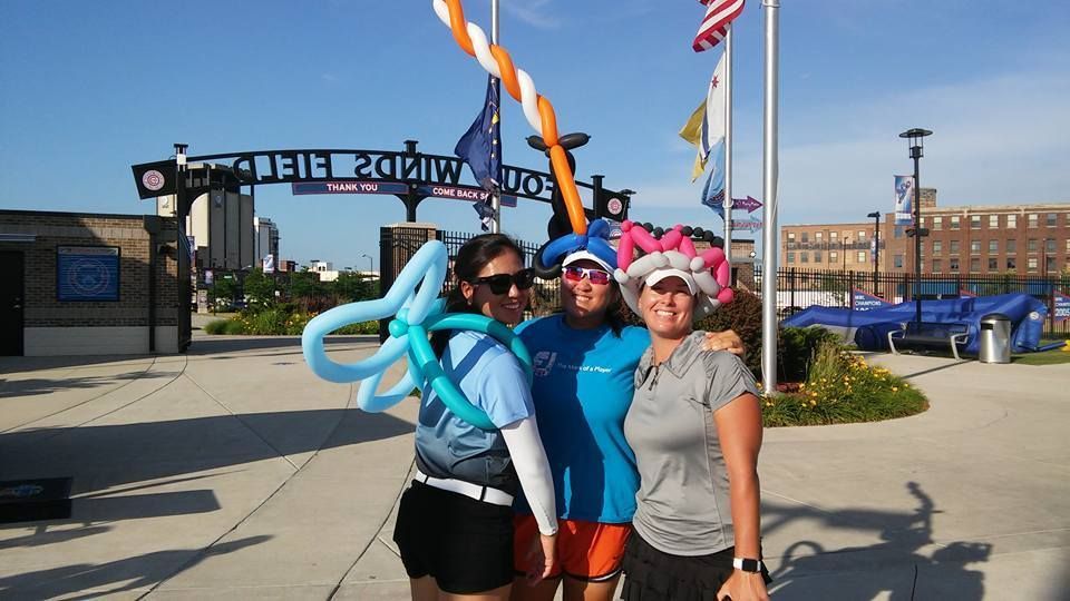 Three women are posing for a picture wearing twisted balloon hats at Four Winds Field