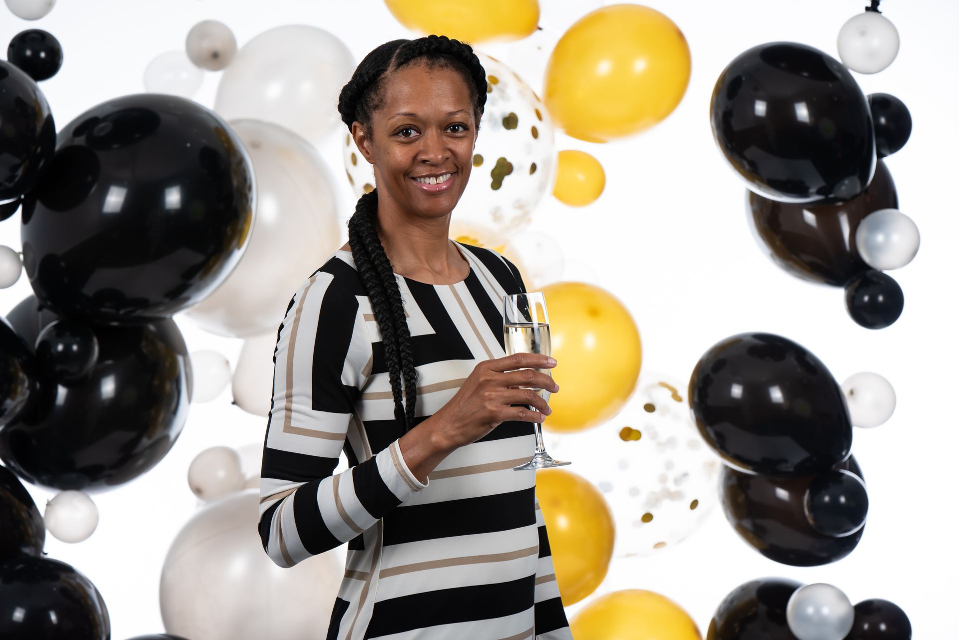 A woman is holding a glass of champagne in front of balloons.