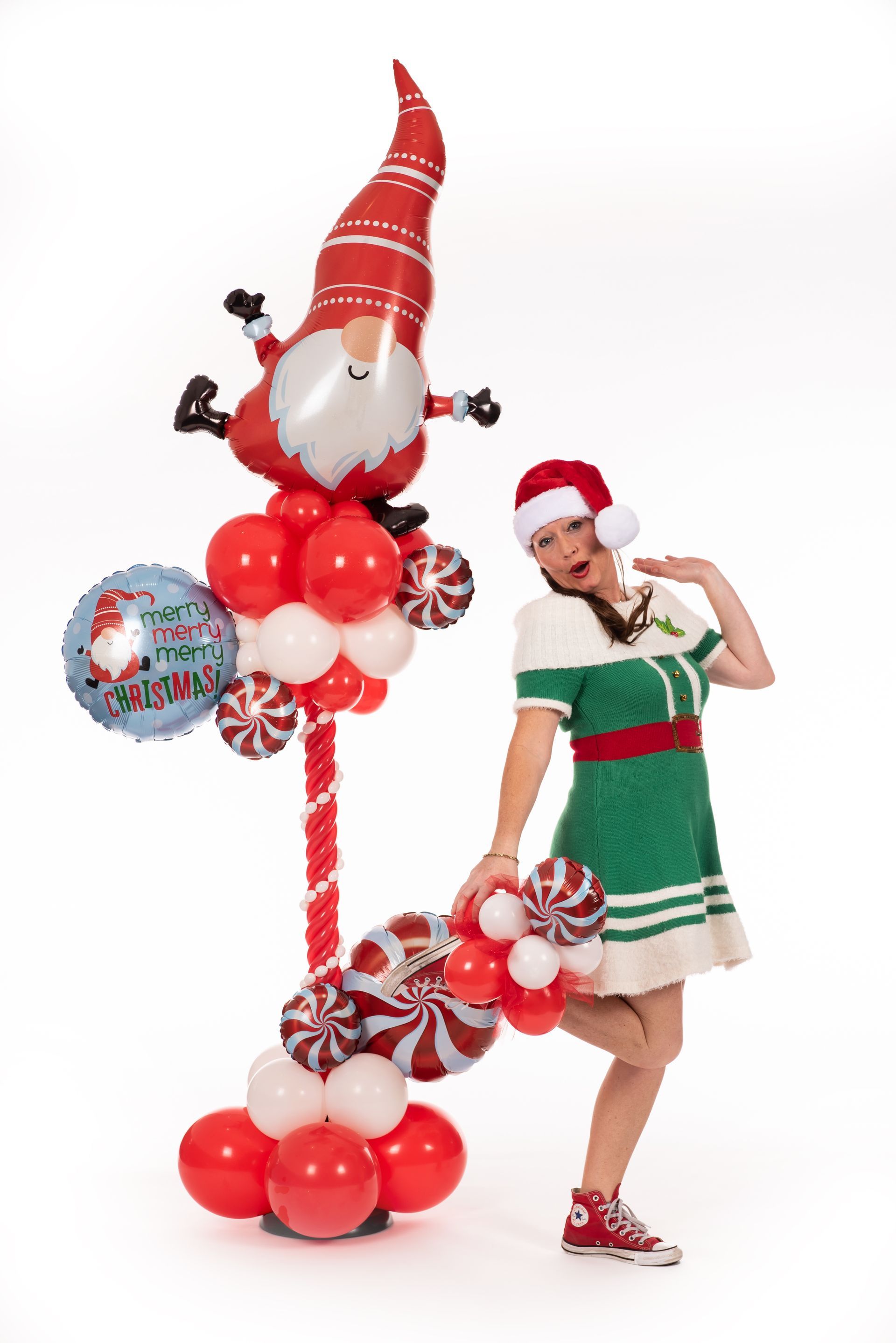 A woman dressed as an elf is standing next to a balloon display.