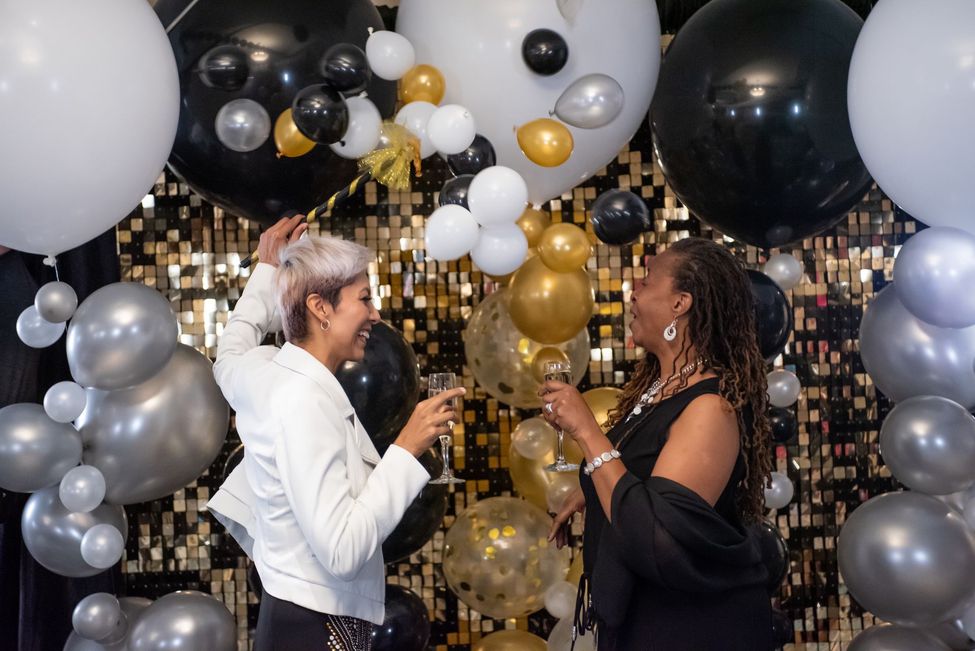 Two women are standing in front of a wall of balloons.