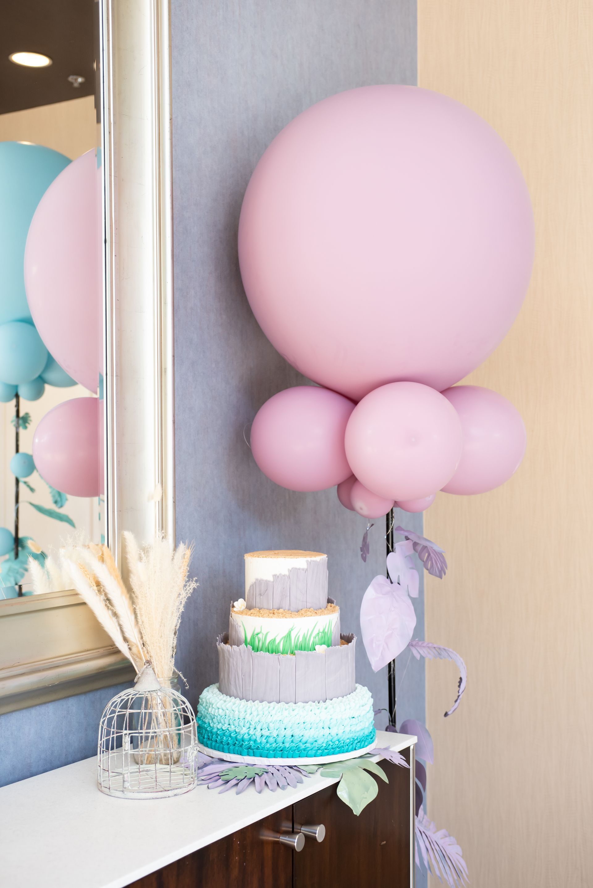 A cake is sitting on a table next to a mirror and balloons.