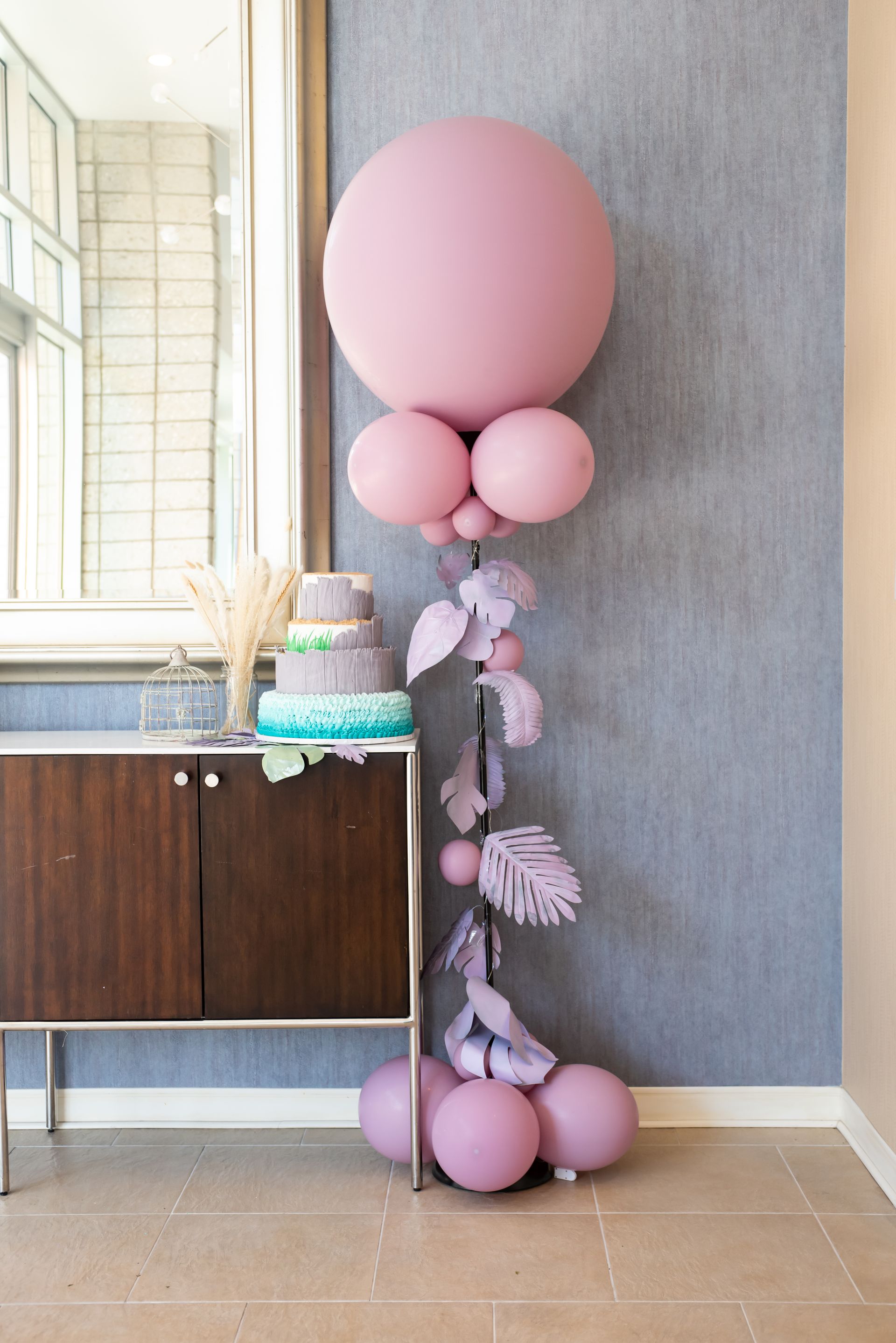 A bunch of pink balloons are sitting on a table next to a cake.