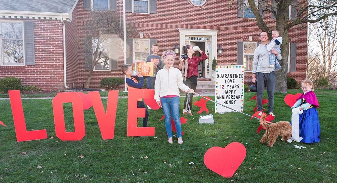 A family is standing in front of a house with a sign that says `` love ''.