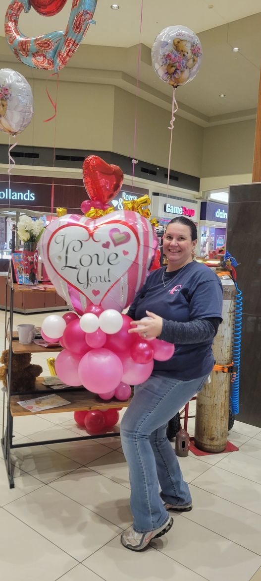 A woman is holding a heart shaped balloon in a store.