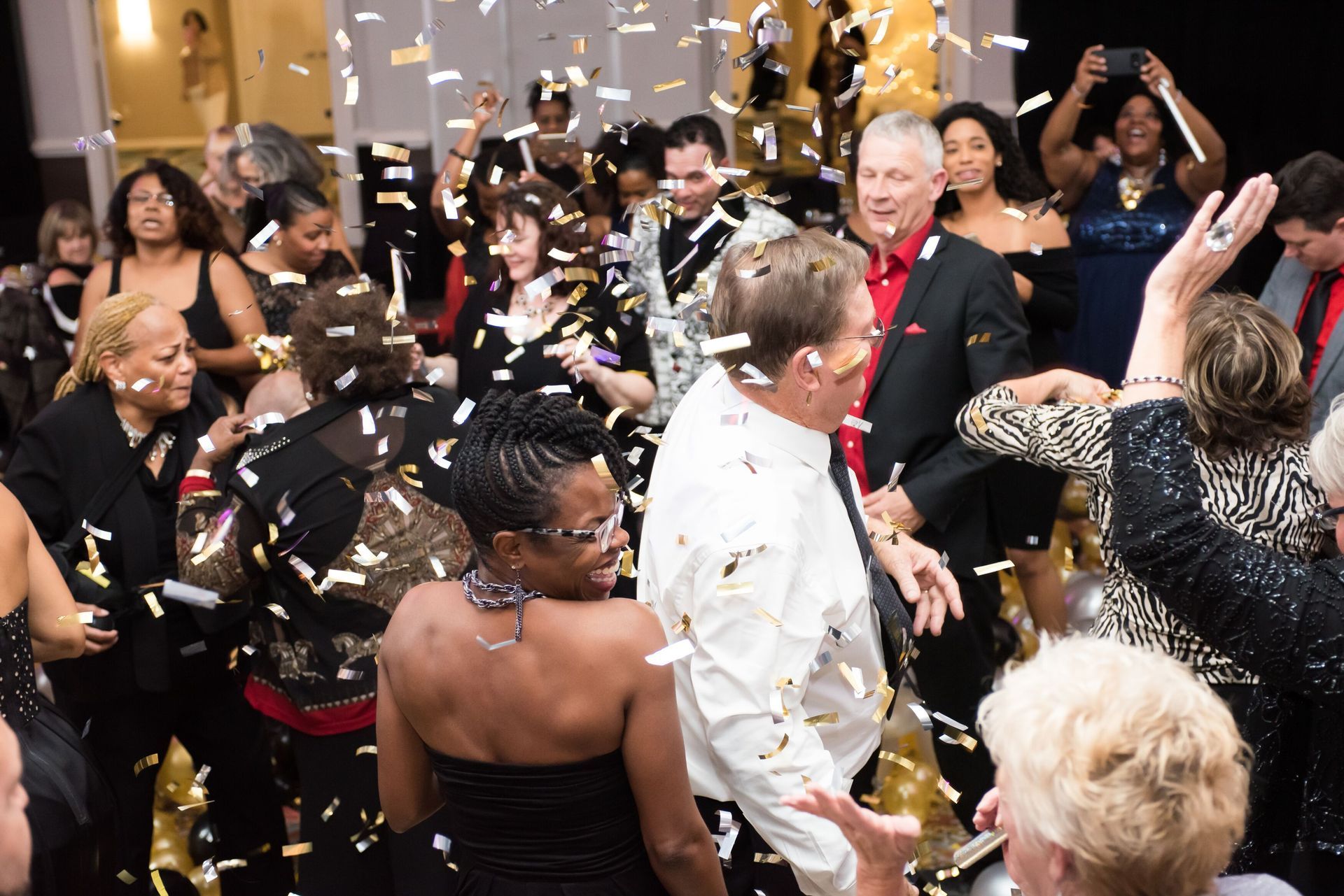 A crowd of people are dancing in a room with confetti falling. Balloon Drop