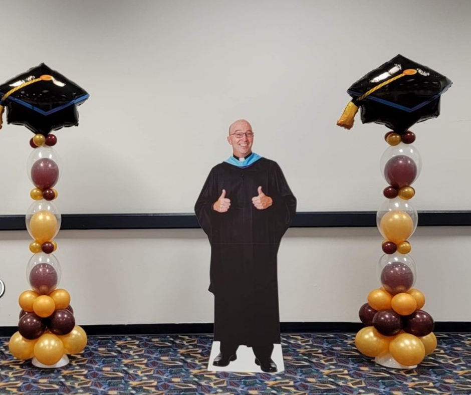 A cardboard cutout of a man in a graduation cap and gown giving a thumbs up