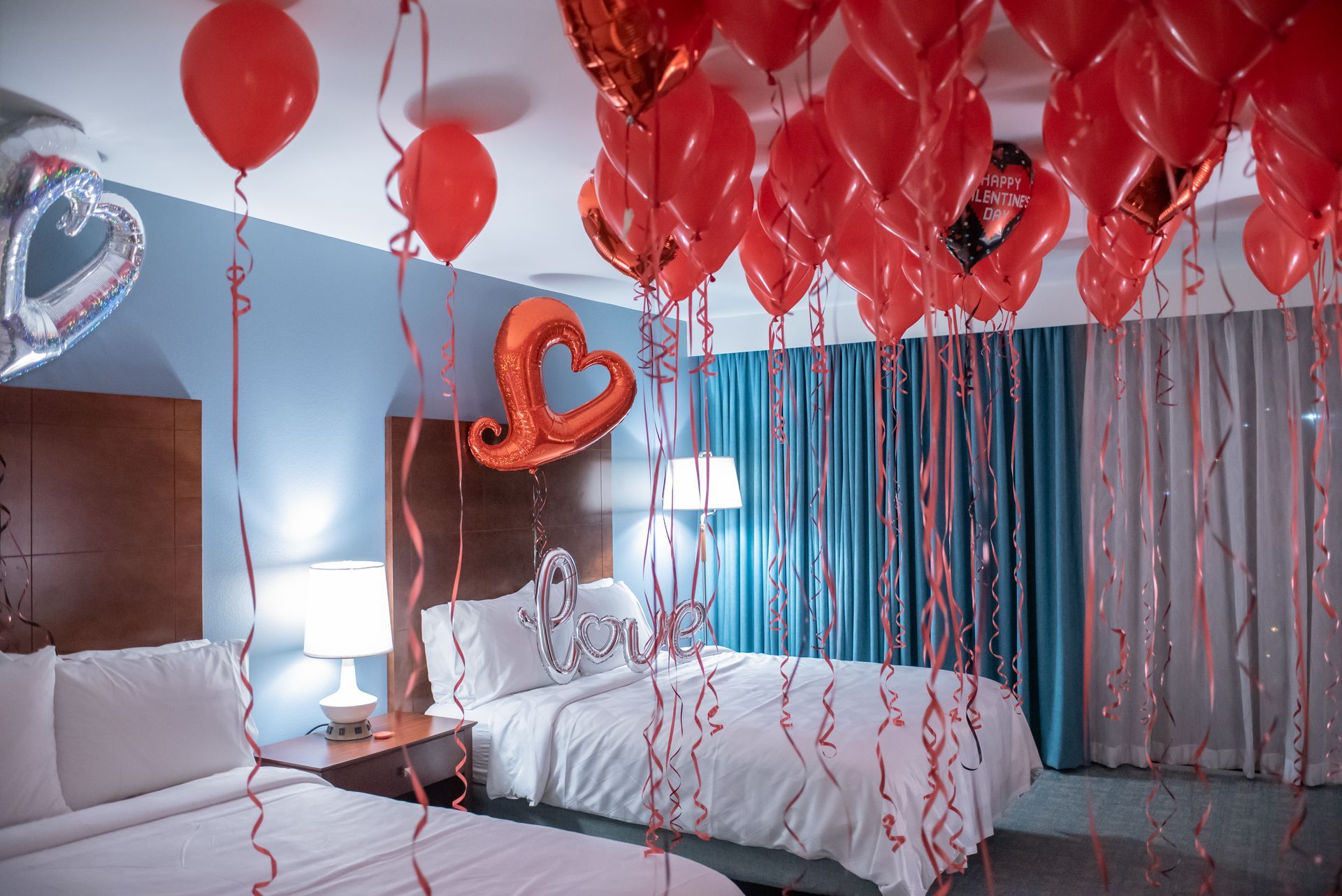 A hotel room decorated for valentine 's day with red balloons hanging from the ceiling.