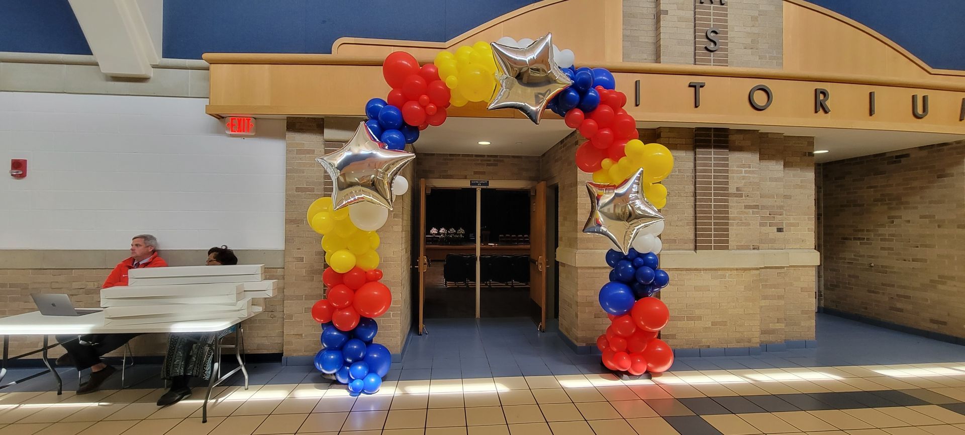 A red , yellow , and blue balloon arch is in front of a building.