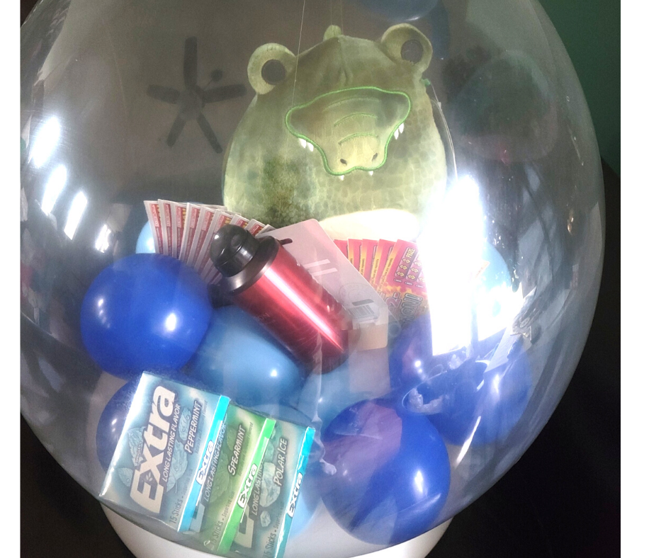 A stuffed frog is in a clear balloon filled with balloons and extra gum