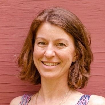 Woman with short brown hair smiles, red wall background.