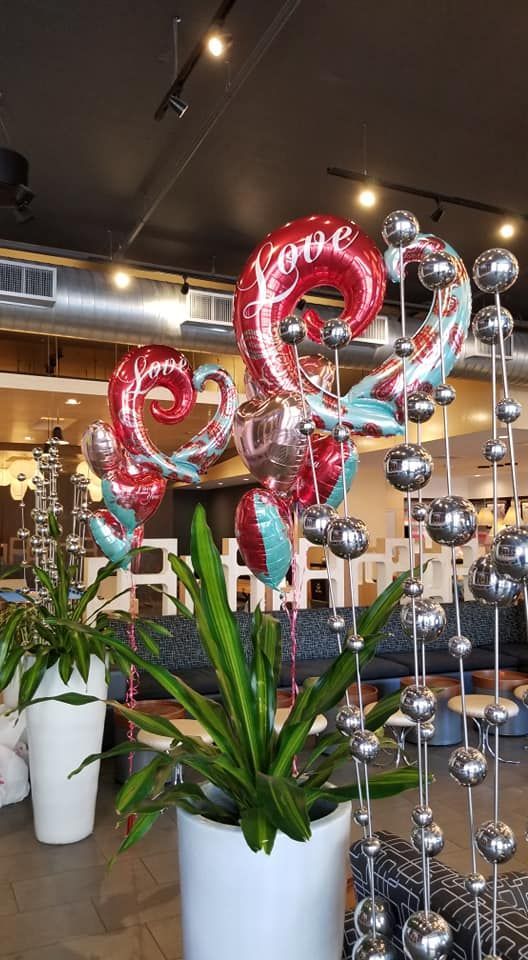 A bunch of heart shaped balloons are sitting on top of a potted plant.