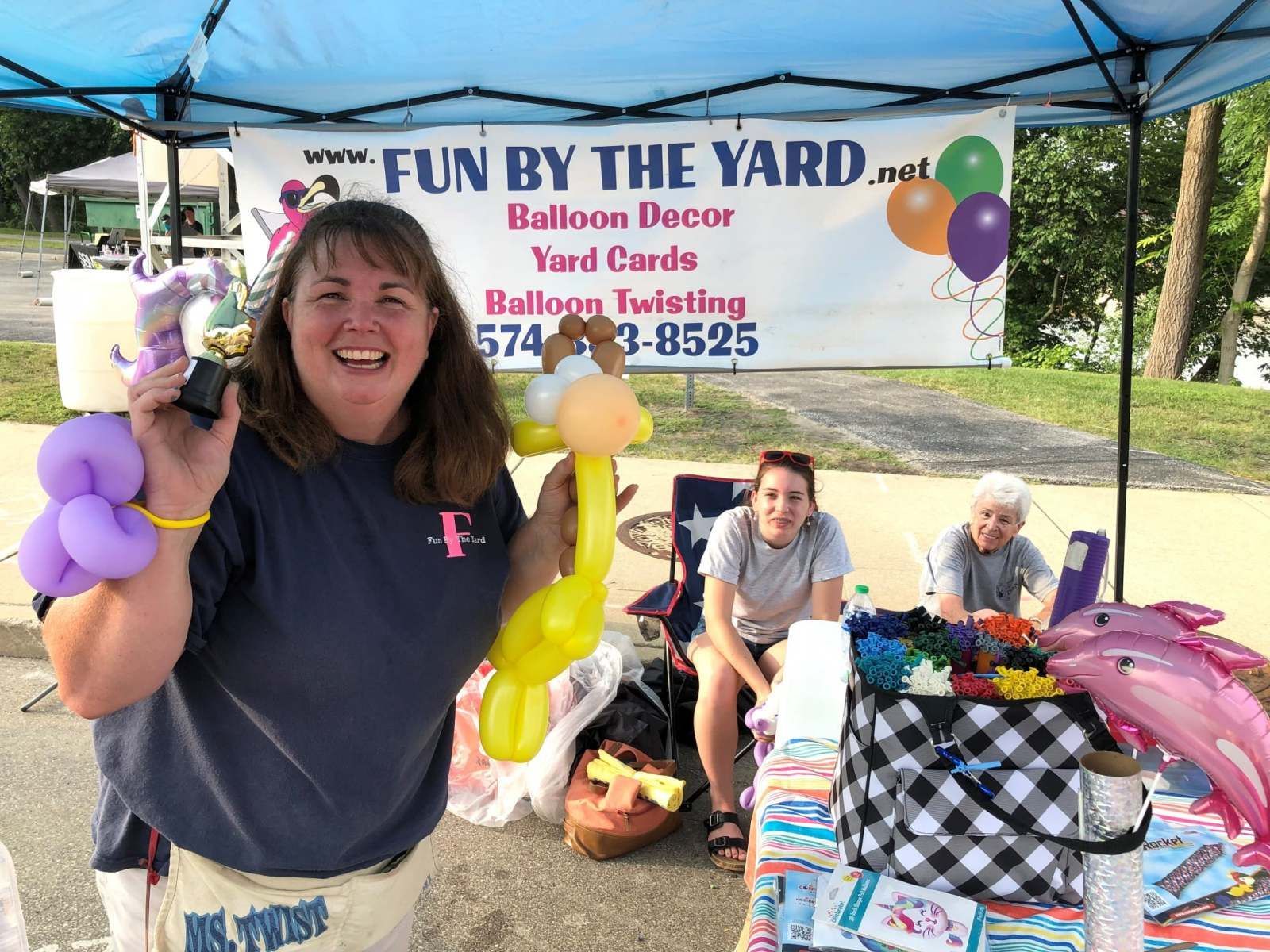 A woman is holding balloons in front of a sign that says fun by the yard