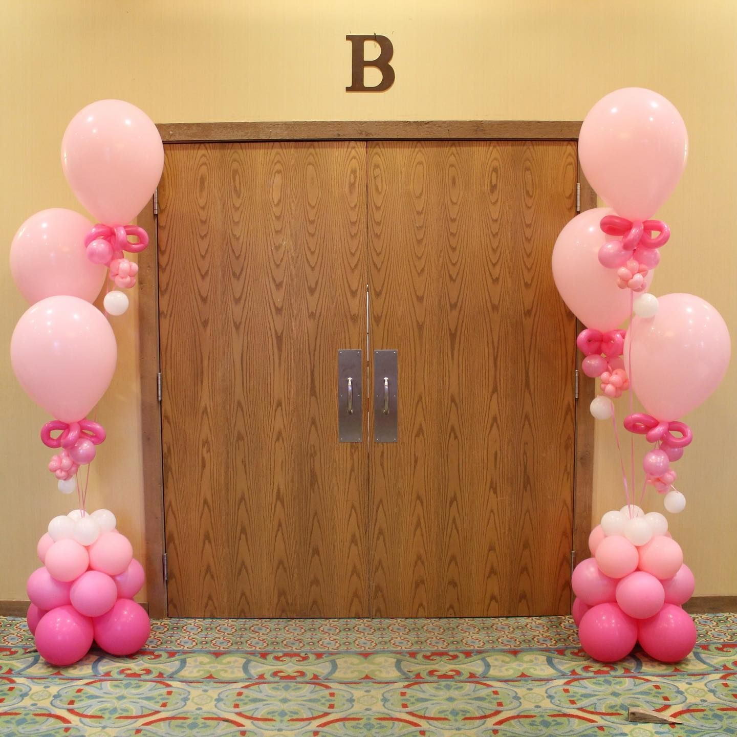 Pink balloons are lined up in front of a door with the letter b above it